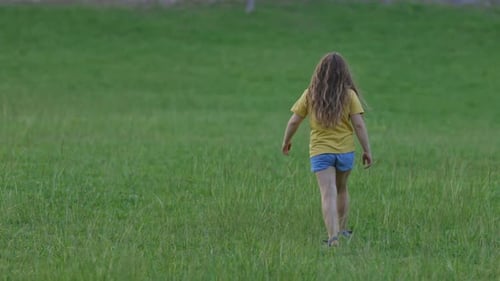 Young Girl Walking Away in a Green Field