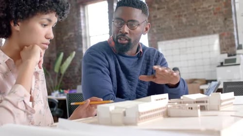 Focused diverse architect colleagues discussing work with building model in office in slow motion