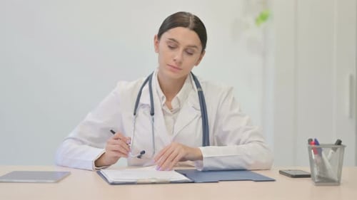 Female Doctor Writing at Desk in Office