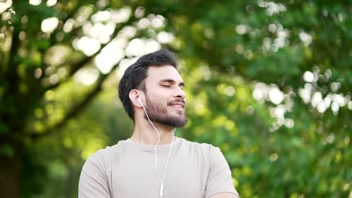 Happy sportsman with headphones relaxing with closed eyes standing in urban city park. Smiling hands