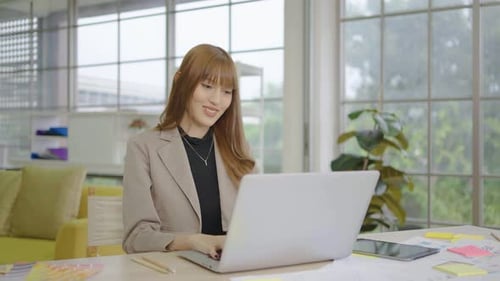 Young asian business woman thinking and typing on laptop computer working in internet at office