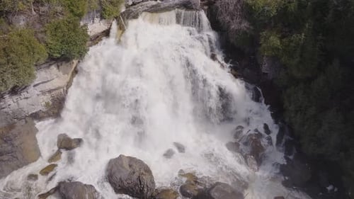 Powerful waterfall cascading over rocks surrounded by lush green trees, aerial view