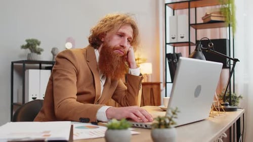 Bored Sleepy Tired Businessman Worker Working on Laptop Computer Leaning on Hand at Home Office Desk