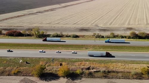 Multiple Semitrucks and Cars Traveling Along a Busy Highway Surrounded By Flat Agricultural Fields
