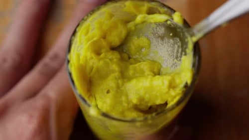 Scooping Mixing Yellow Avocado Puree With Spoon Into Glass Pot, Close Up
