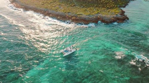 Catamaran sailing along turquoise sea near rocky tropical coastline in sunlight