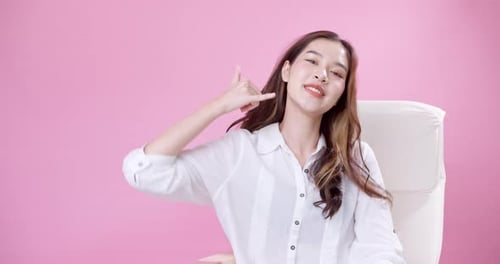 Young Asian woman making phone call motion with hands in the studio with pink background