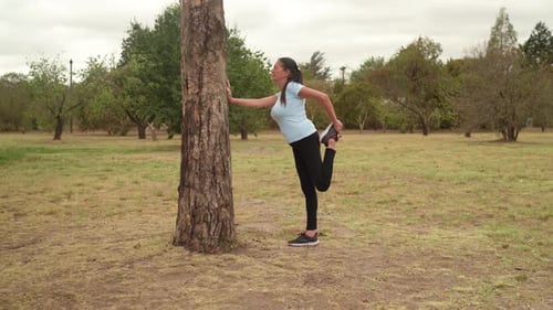 Woman Stretching Quads Holding Tree in Park