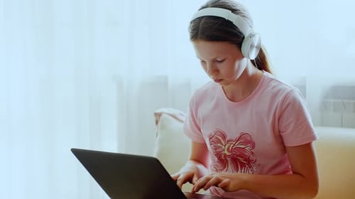 Girl Typing on Laptop Wearing Headphones at Home