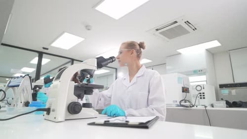 Female Scientist Works with Microscope in Bright Lab