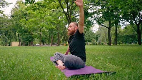 handsome bearded man meditating in the park practicing yoga doing stretching and exercises