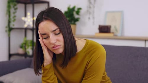 Young Pretty Woman Suffering From Headache Sitting on Sofa at Home