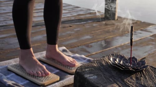 Frau steht auf einem Sadhu-Brett mit Weihrauch am Wasser