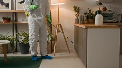 Arbeiter im Schutzanzug verwendet ein Sprühgerät zur Dekontamination im häuslichen Raum