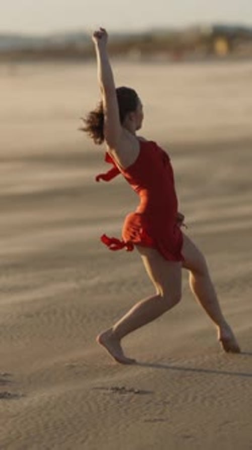 Graceful Young Woman in Red Dress Dancing on Sandy Beach