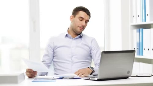 Busy hispanic businessman works with laptop and financial papers in office