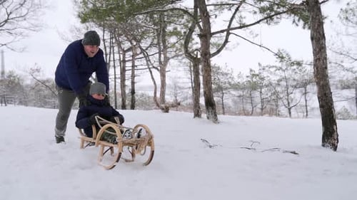 Father Launches Son Pushing Sled Down the Hill on Snowy Winter Day in Park Boy Sledge Outdoors Happy