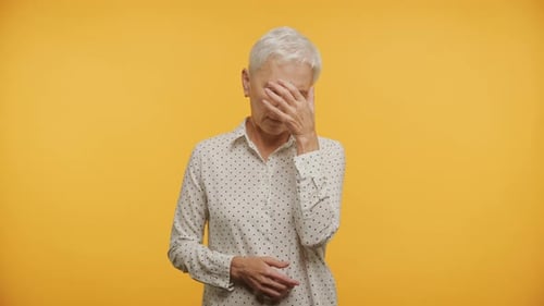 Senior Woman Expressing Sadness on Bright Yellow Background