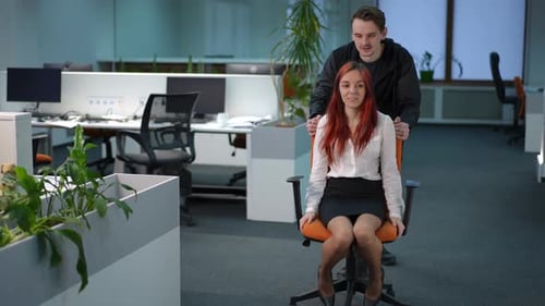 Smiling Man Rolling Office Chair with Cheerful Young Woman in Office Leaving in Slow Motion
