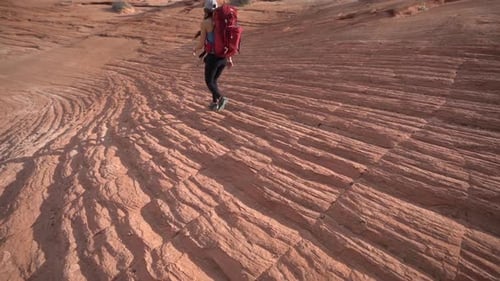 Back of Female Hiker With Backpack Walking on Rocky Sandstone Patterns in Desert of Utah, Cosmic Ash