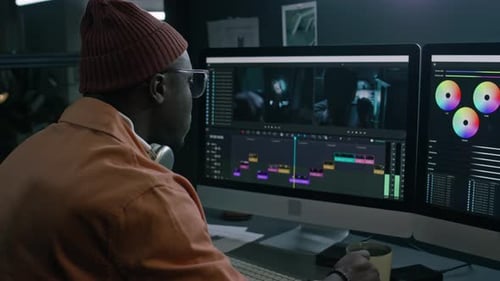 Man Using Computer With Dual Screens in Dark Workspace