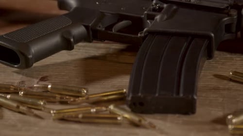 Close dolly out of AR-15 trigger and magazine with ammo scattered around on wooden surface