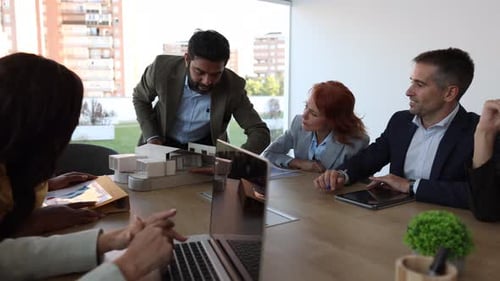 Architects present a model house to their colleagues in a modern office, engaging in a discussion ab