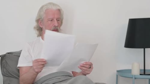 Confused Senior Man Reading Papers in Bed