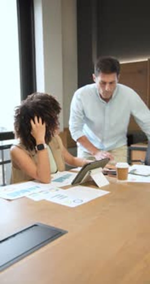 Diverse coworkers arriving with coffee pointing tablet while studying charts together in office