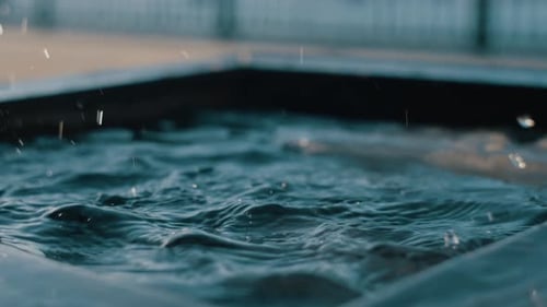 Water Droplets Falling Onto Smooth Dark Surface Creating Spreading Ripples and Soft Splashes with