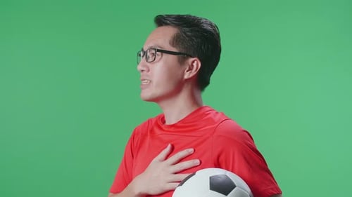Close Up Of Asian Man With A Ball Singing National Anthem While Cheering Soccer On Green Screen