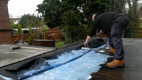Repairman Painting Roof with Blue Paint on House