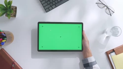 Top down view of man's hand using a mock up green screen tablet on a white desk