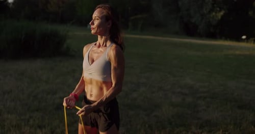 Woman Exercises with Resistance Band Outdoors at Sunset