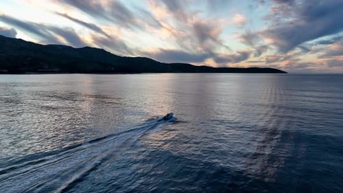 Kleines Motorboot, das bei Sonnenuntergang über das offene Meer rast, mit Dramatisch Wolkenstreifen
