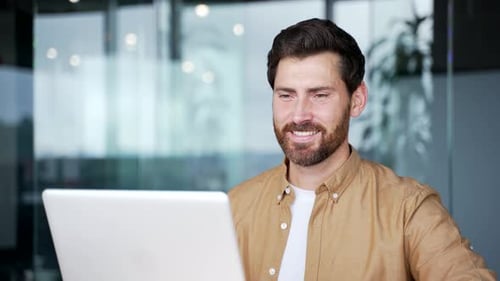 Happy handsome businessman working on a laptop computer sitting at workplace in business office.