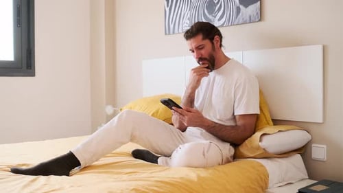 Man Relaxing on Bed Using Cellphone
