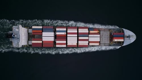 Topdown Aerial View of Container Ship Cutting Through Dark Water Leaving White Wake Cargo Vessel in