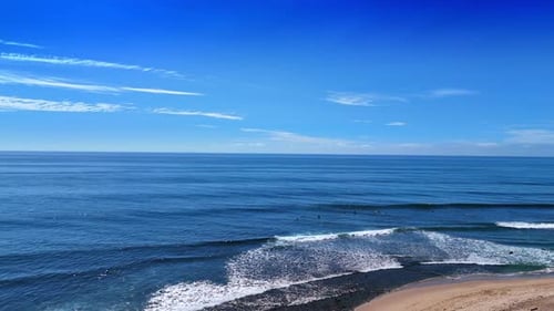 White foamy waves roll to the coast. Surfers are practicing in the Pacific Ocean on sunny day.