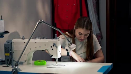 in the Sewing Workshop Young Girl Works with a Sewing Machine and White Fabric