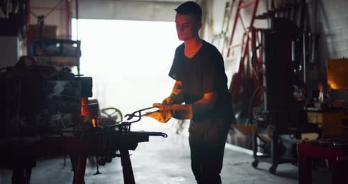 Male Craftsman Looking and Taking a Piece of Red Hot Metal In