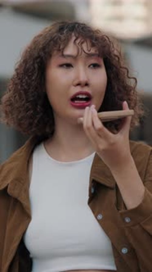 Modern Woman Recording Voice Message On Phone While Standing In City Center