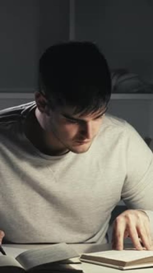 Young Adult Studying and Writing in Dimly Lit Room