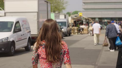 back view of a brown hair woman in colorful dress walking down the street of the market-place. slowm