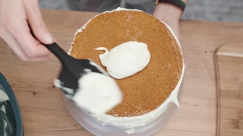 Top-down view of a woman spreading a layer of cream around the edges of a sponge cake.