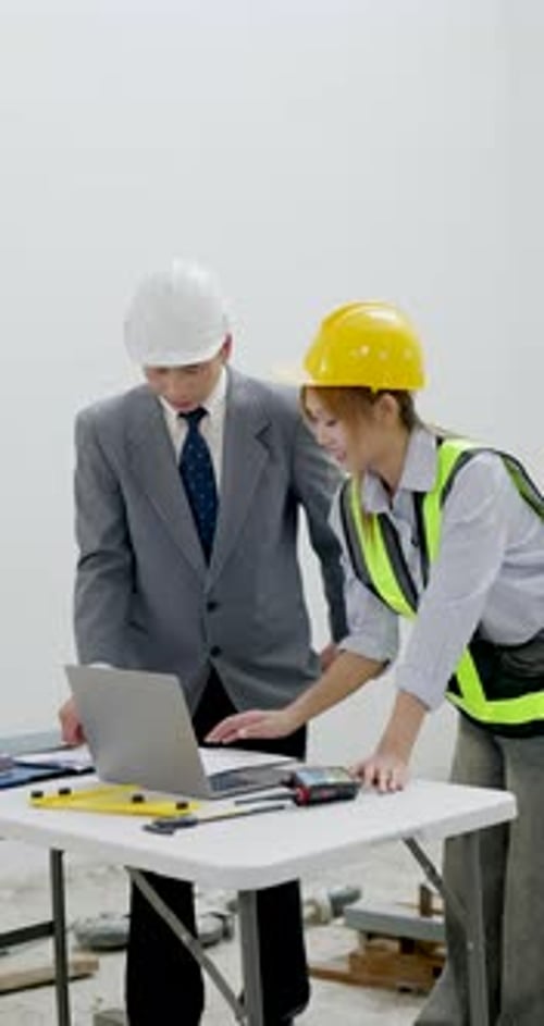Asian male construction manager and woman engineer compare blueprint with laptop data, coordinating