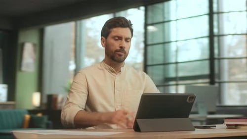 Portrait of Serious Man Sitting at Desk Use Tablet Computer Work in Office Thinking Camera Moving