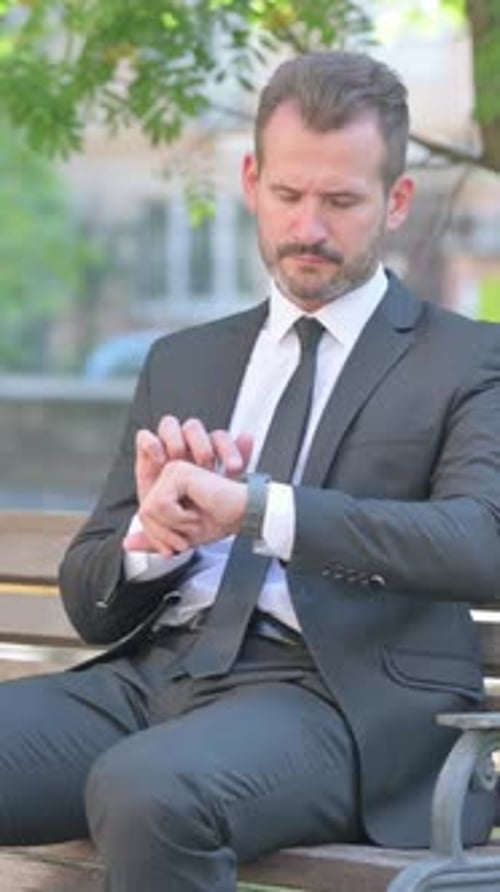 Man in suit checks watch while sitting on bench