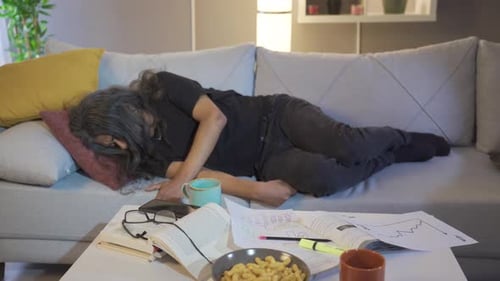 Exhausted Man Lying on Couch Surrounded by Work