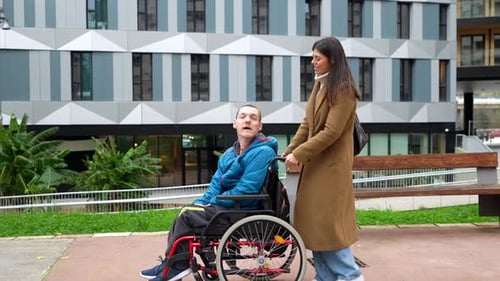 Woman Pushes Man in Wheelchair Along Urban Sidewalk